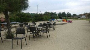 An outdoor seating area with tables and chairs, surrounded by sand and greenery. - Hotel Club Torre Marino (Ricadi)