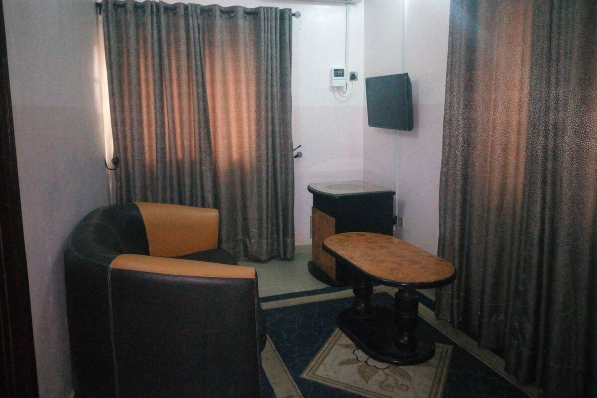 A small, dimly lit room with a single leather armchair, a small table, and a television mounted on the wall.