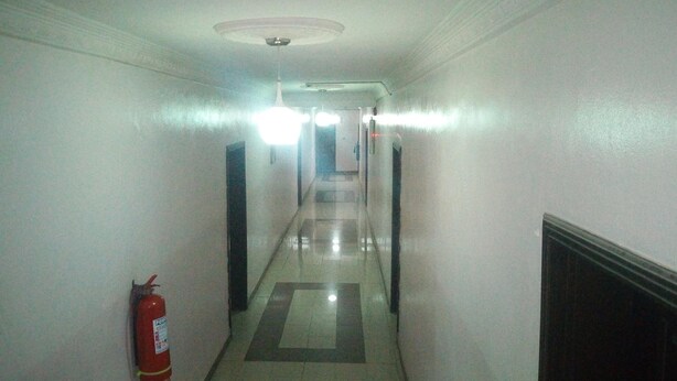 A long, narrow hallway with a fire extinguisher on the left wall, a ceiling light, and a door at the end. - Bayse One Executive Suites and Bar (Ibadan)