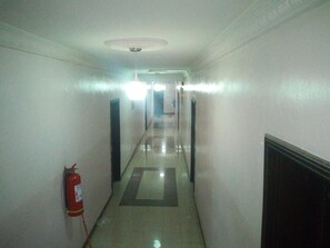 A long, narrow hallway with a fire extinguisher on the left wall, a ceiling light, and a door at the end. - Bayse One Executive Suites and Bar (Ibadan)