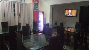 A dining area with a glass table and chairs, a Coca-Cola refrigerator, and a television mounted on the wall. - Bayse One Executive Suites and Bar (Ibadan)