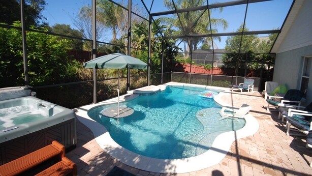 A covered outdoor swimming pool with hot tubs, lounge chairs, and a pergola with an umbrella.