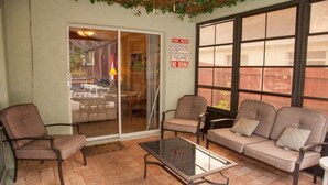 A patio area with a glass door leading to an outdoor dining space, a cushioned sofa, and a glass coffee table.