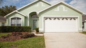 A light green single-story house with a white garage door, a small front porch, and a well-maintained lawn.