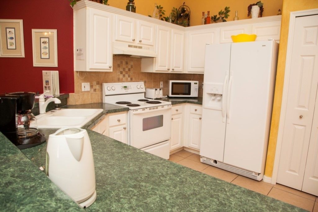 A kitchen with white cabinets, a stove, a microwave, and a refrigerator.