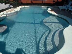 A clear swimming pool with a tiled deck and a wooden fence in the background.