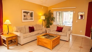 A living room with two beige sofas, a wooden coffee table, a side table, a lamp, and a framed picture on the wall.