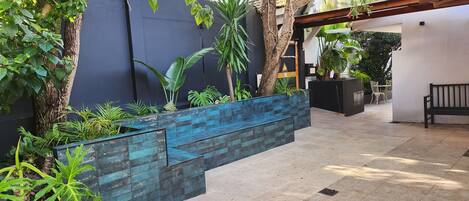A covered outdoor area with a tiled floor, a blue planter wall, and various plants.