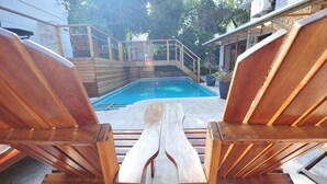 Una terrassa de fusta amb dues gandules orientades cap a una piscina, tot t'hi envolten una tanca de fusta i plantes en testos.