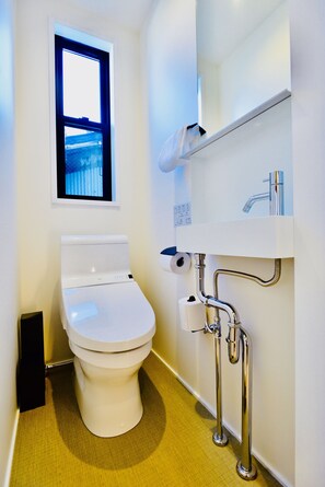 Un baño moderno con inodoro, ventana y lavamanos con espejo.