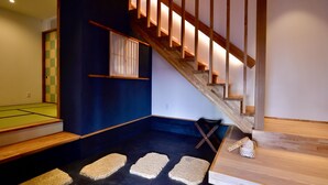 A modern interior with a wooden staircase, a dark blue wall, and a small seating area with a cushion and a bag. - Cochi-en (Kyoto)