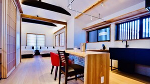 A modern hotel room with a wooden ceiling, a dining area with red chairs, and a kitchen with a blue countertop. - Cochi-en (Kyoto)