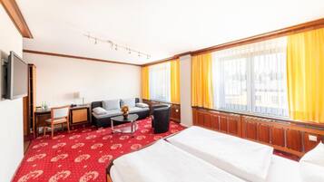 A hotel room with a bed, a desk, a chair, a sofa, and a TV.