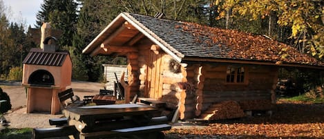 A rustic log cabin with a chimney, a wooden bench, and a picnic table in front.