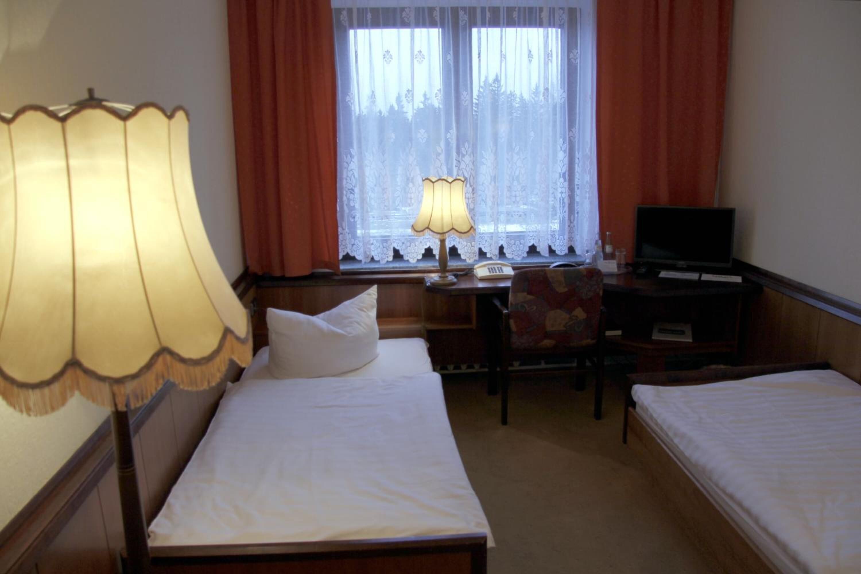 Habitación de hotel con dos camas individuales, un escritorio con lámpara, una silla y un televisor.