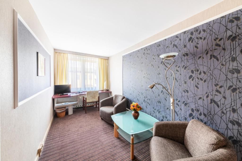 A hotel room with a sofa, a glass coffee table, a TV, a desk, and a chair.