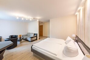 A modern hotel room with a large bed, a sofa, a desk, and a chair. - Hotel Forstmeister (Schoenheide)