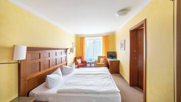 A hotel room with a large bed, a desk, a chair, a TV, and a window with curtains.