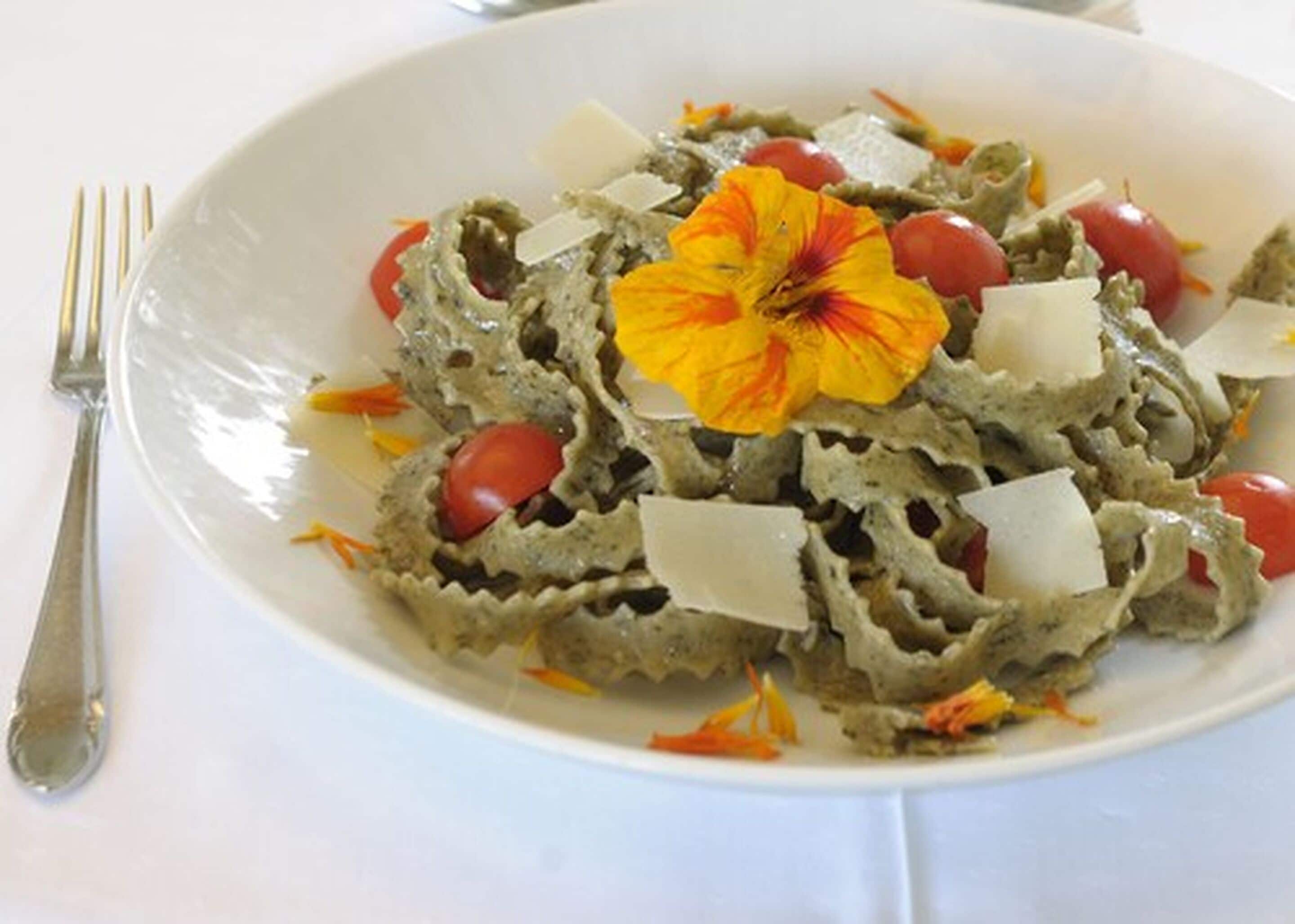 A plate of pasta with cherry tomatoes and a flower garnish.