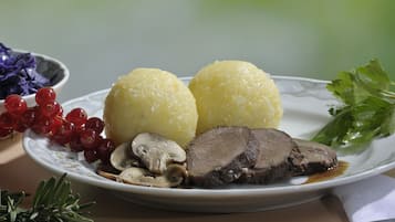 A plate with two round yellow dumplings, sliced beef, mushrooms, red currants, and a sprig of rosemary.