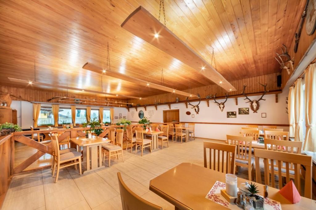 A wooden interior with multiple dining tables and chairs, a high ceiling with exposed beams, and antler decorations on the walls.