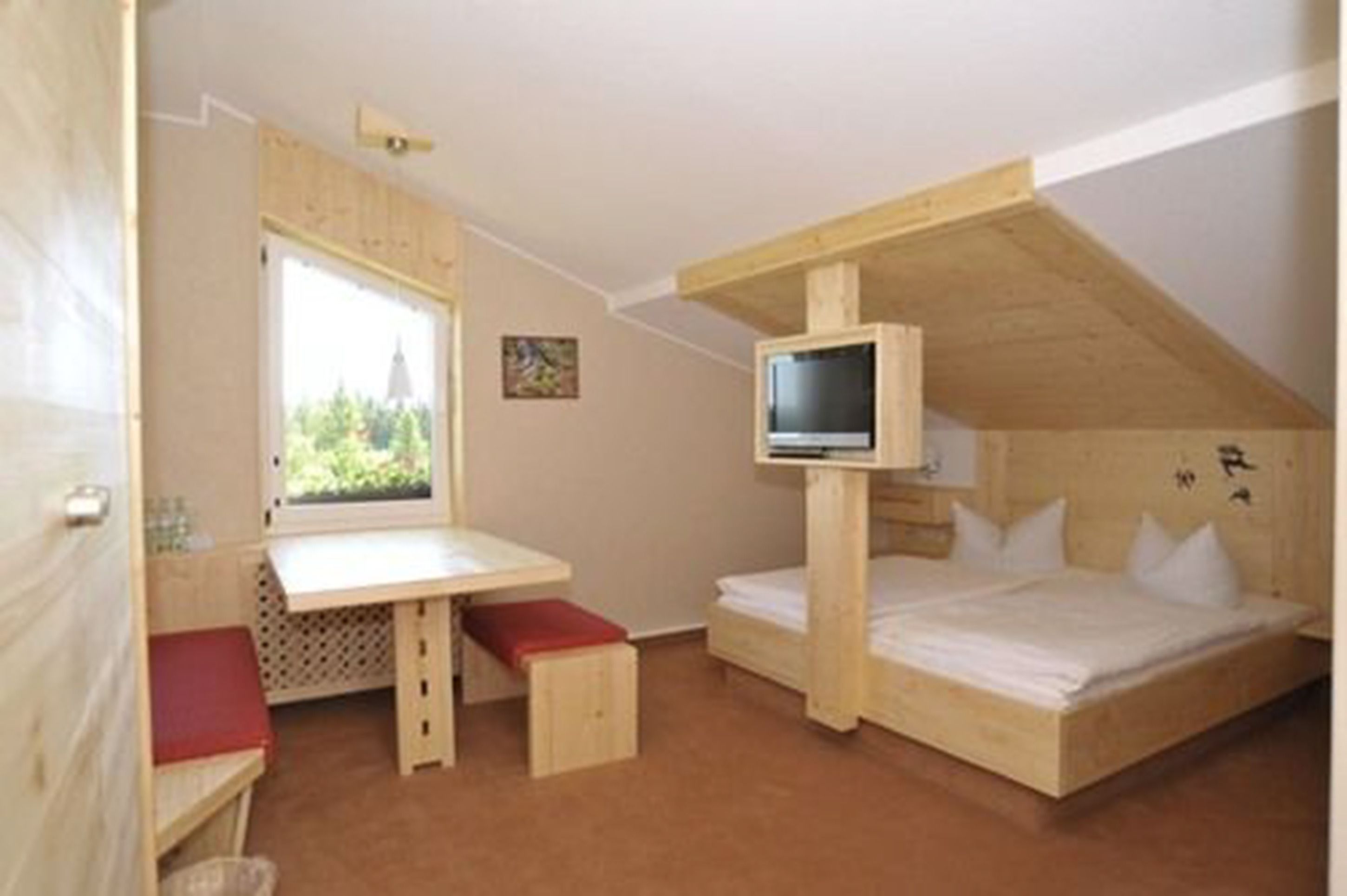 A compact room with a loft bed, a small desk, and a television.