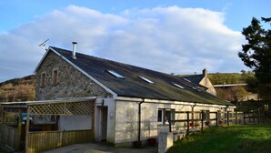 A stone building with a sloped roof, a fenced area, and a small porch. - Gilfach Wen Barn (Carmarthen)