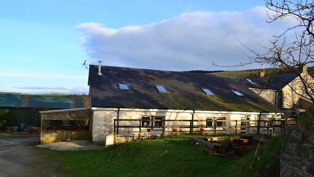 A two-story building with a sloped roof, multiple windows, and a fenced outdoor area. - Gilfach Wen Barn (Carmarthen)
