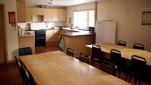 A compact kitchen with wooden cabinets, a stove, and a dining area with a table and chairs. - Gilfach Wen Barn (Carmarthen)