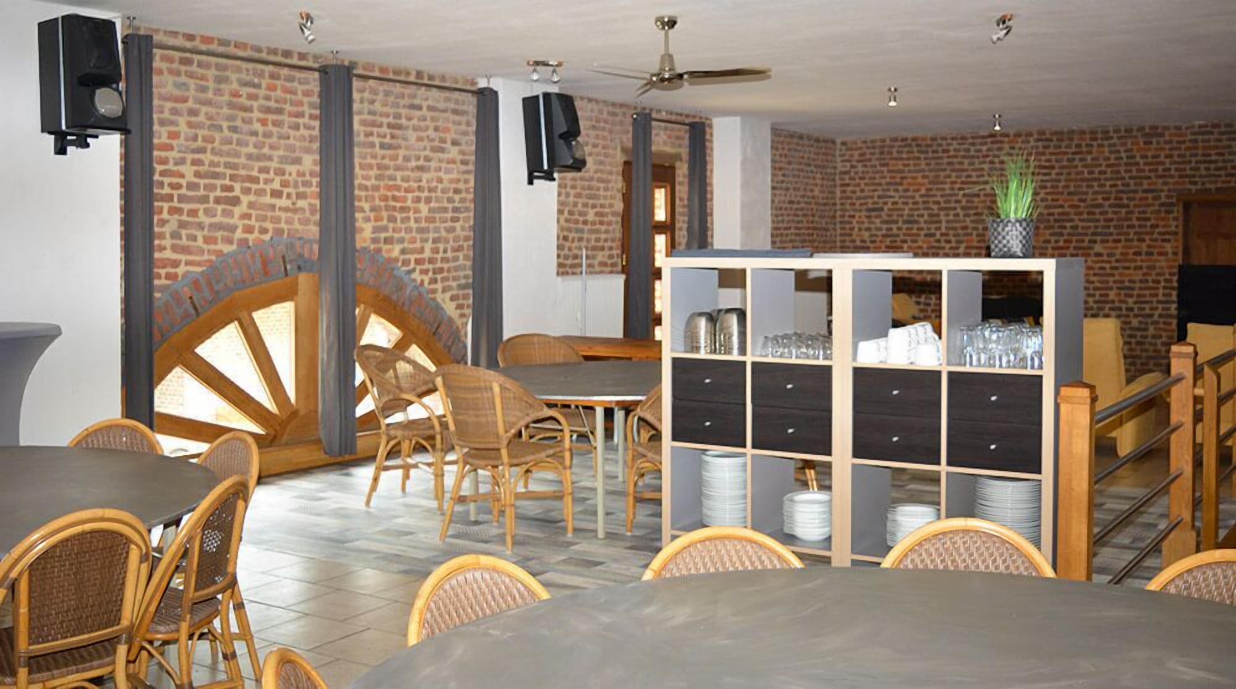 Restaurante com paredes de tijolo, mesas e cadeiras de madeira, uma grande estrutura circular de madeira e uma vitrine de vidro com pratos.