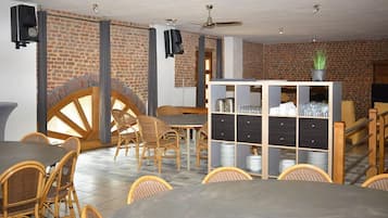 Restaurante com paredes de tijolo, mesas e cadeiras de madeira, uma grande estrutura circular de madeira e uma vitrine de vidro com pratos.