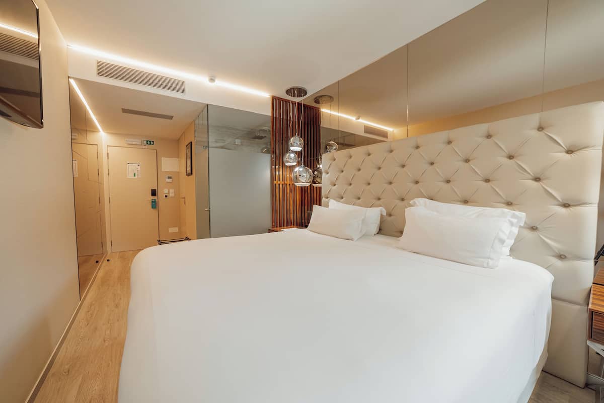 Ett modernt hotellrum med en stor säng, en väggpanel i trä och en glasvägg.