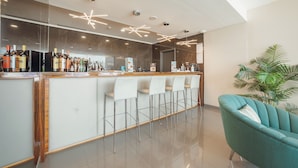 A modern bar area with a long counter, several bar stools, and a teal armchair.