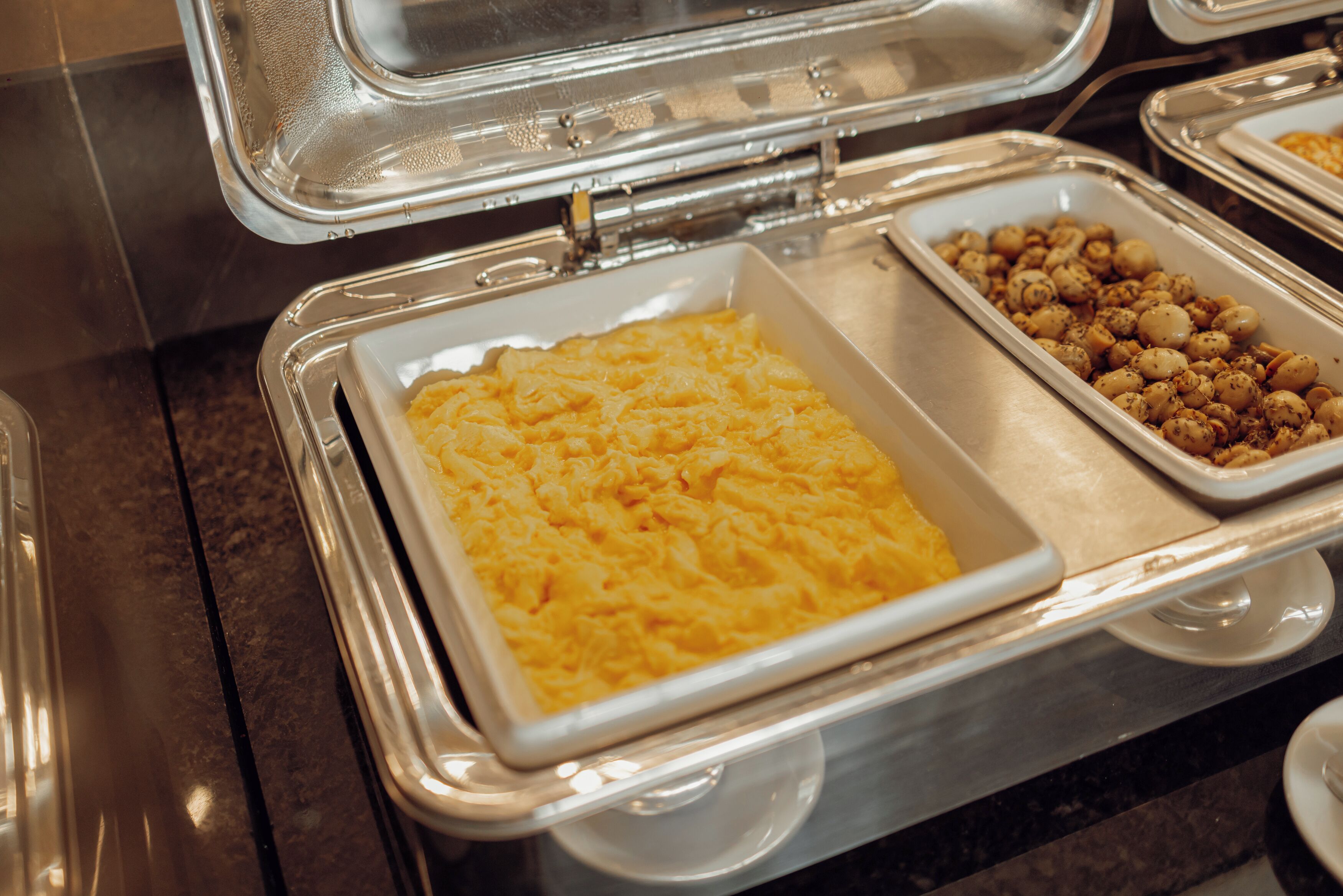 A buffet with various dishes, including scrambled eggs and nuts.