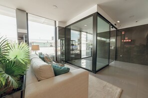 A modern hotel lobby with a glass partition, a sofa with cushions, a lamp, and a potted plant. - ABC Hotel Porto - Boavista (Porto)
