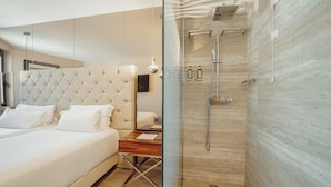 A modern bedroom with a tufted headboard, a bedside table, and a glass partition separating the shower area.