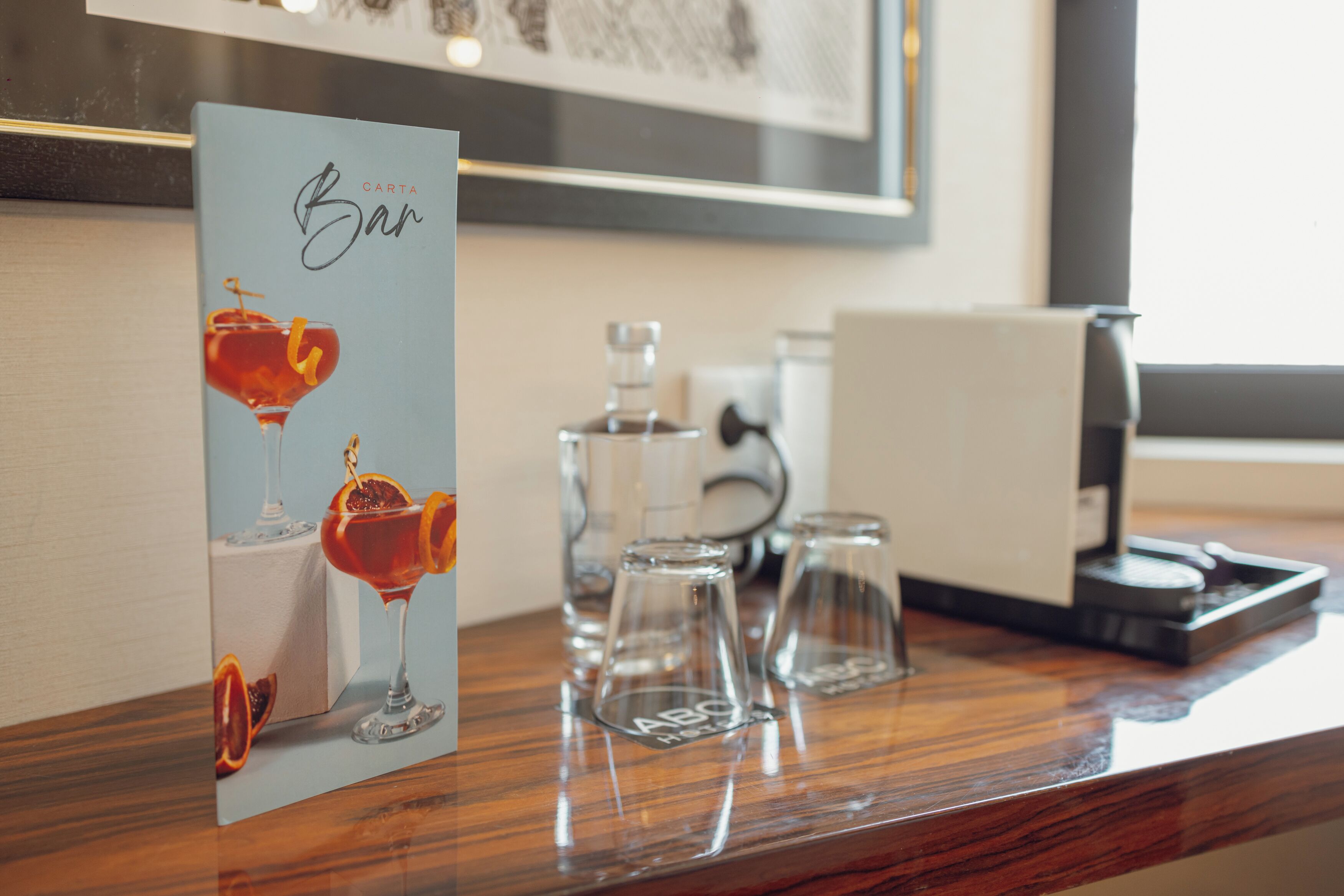 Uma área de bar com uma placa que diz 'CARTA Bar', um copo de bebida vermelha e três copos com etiquetas 'ABO' sobre um balcão de madeira.