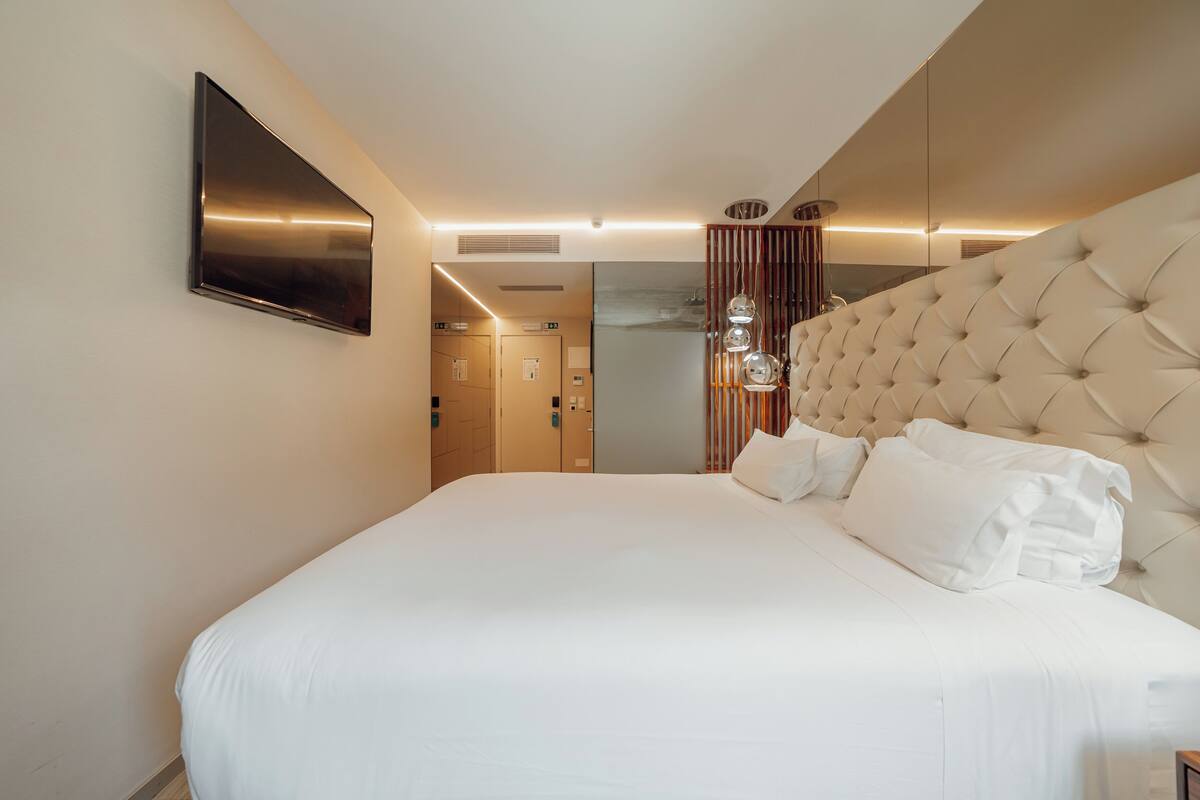 Ett modernt hotellrum med en stor säng, en platt-TV som är monterad på väggen och en dekorativ lampa ovanför sängen.