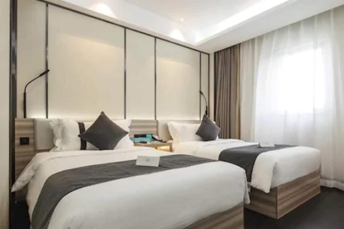 A hotel room with two beds, a large window with curtains, and a modern design.