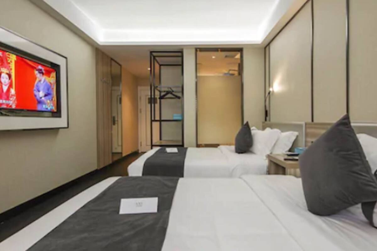 A hotel room with two beds, a TV on the wall, and a wardrobe.