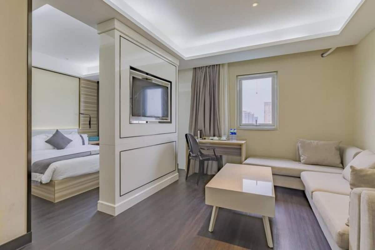 A hotel room with a bed, a desk, a chair, a sofa, and a television.