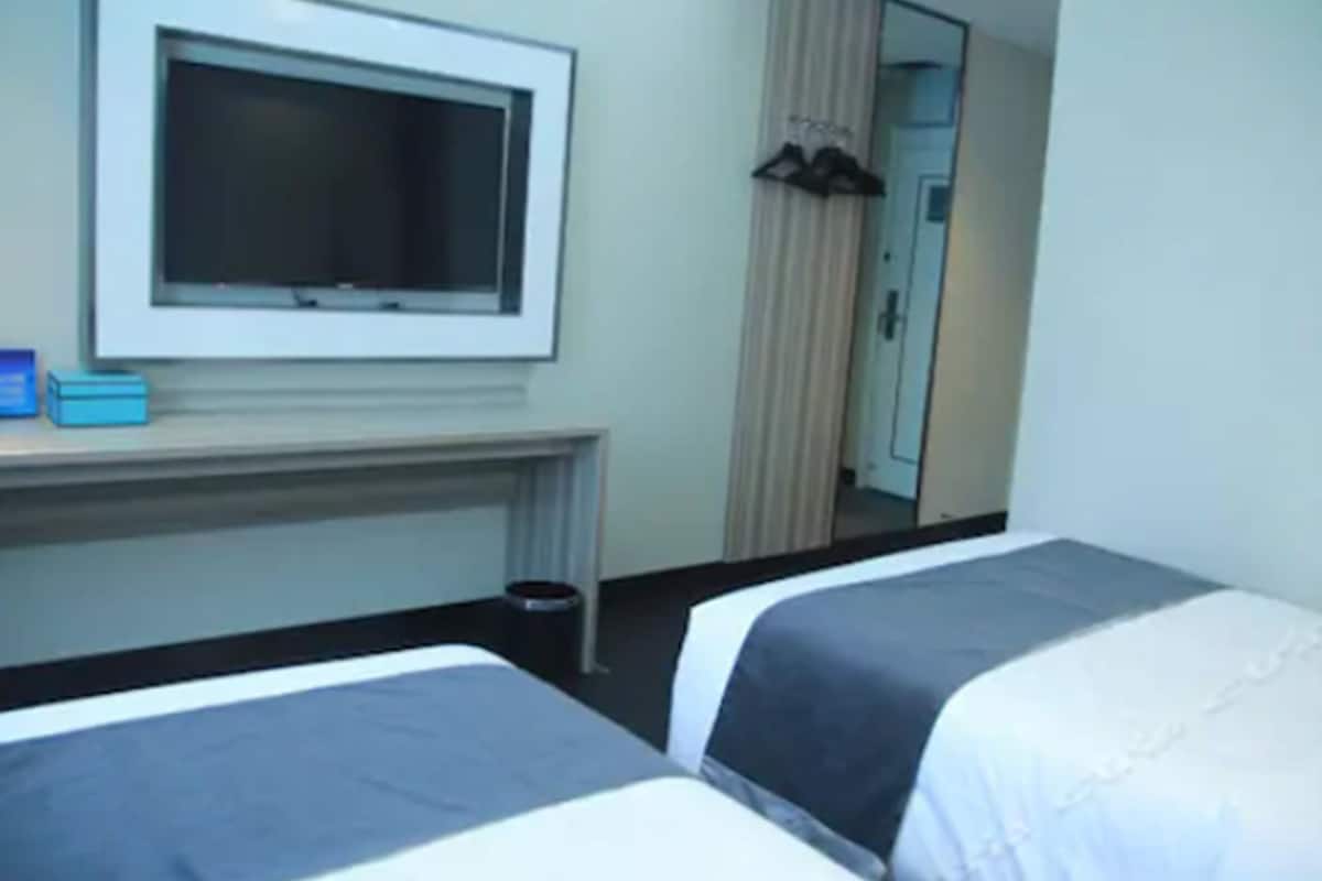 A hotel room with two beds, a TV on a stand, a mirror, and a door leading to a bathroom.