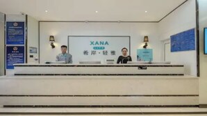 A reception desk with a sign reading "XANA" and two individuals seated behind it. - Xana Lite Hotelle Shunyi (Shunyi)