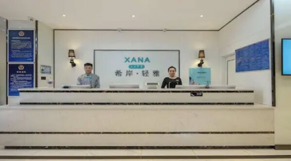 A reception desk with a sign reading "XANA" and two individuals seated behind it.