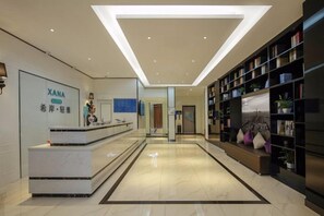 A hotel lobby with a reception desk, a seating area with bookshelves, and a modern ceiling design.
