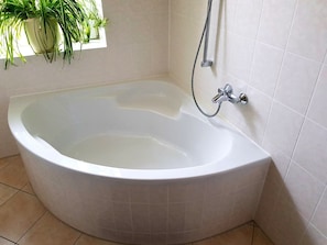 A corner bathtub with a shower head and a potted plant. - Apartment on the Elbe Ferry - Apartment for 2 - 3 People (Dresden)