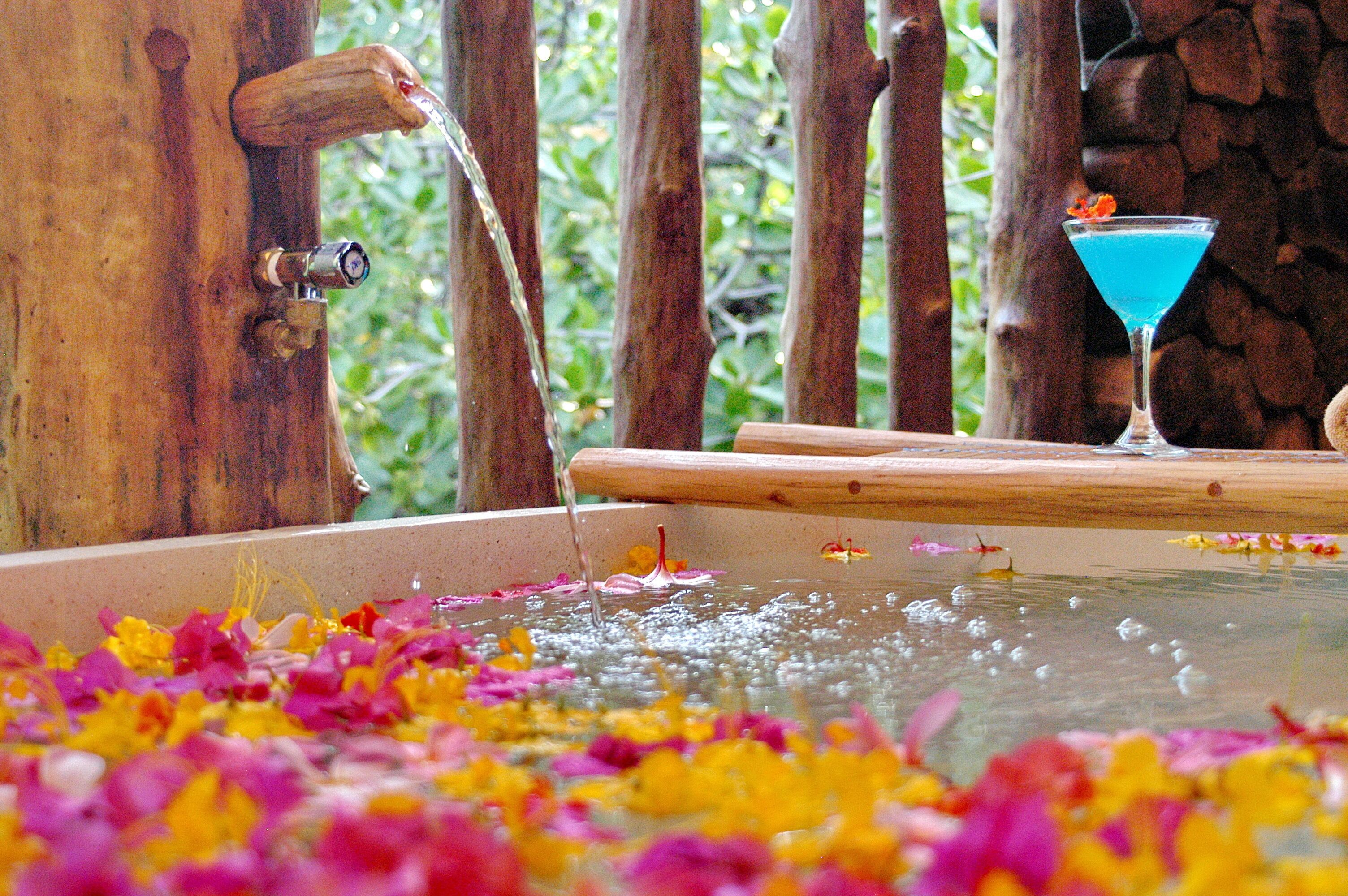 A wooden water feature with a fountain, a martini glass with a blue drink, and colorful flower petals in the water.