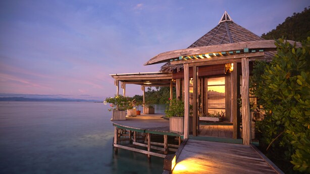 A wooden structure with a thatched roof overlooking a calm body of water. - Raja Ampat Dive Lodge (Mansuar Island)