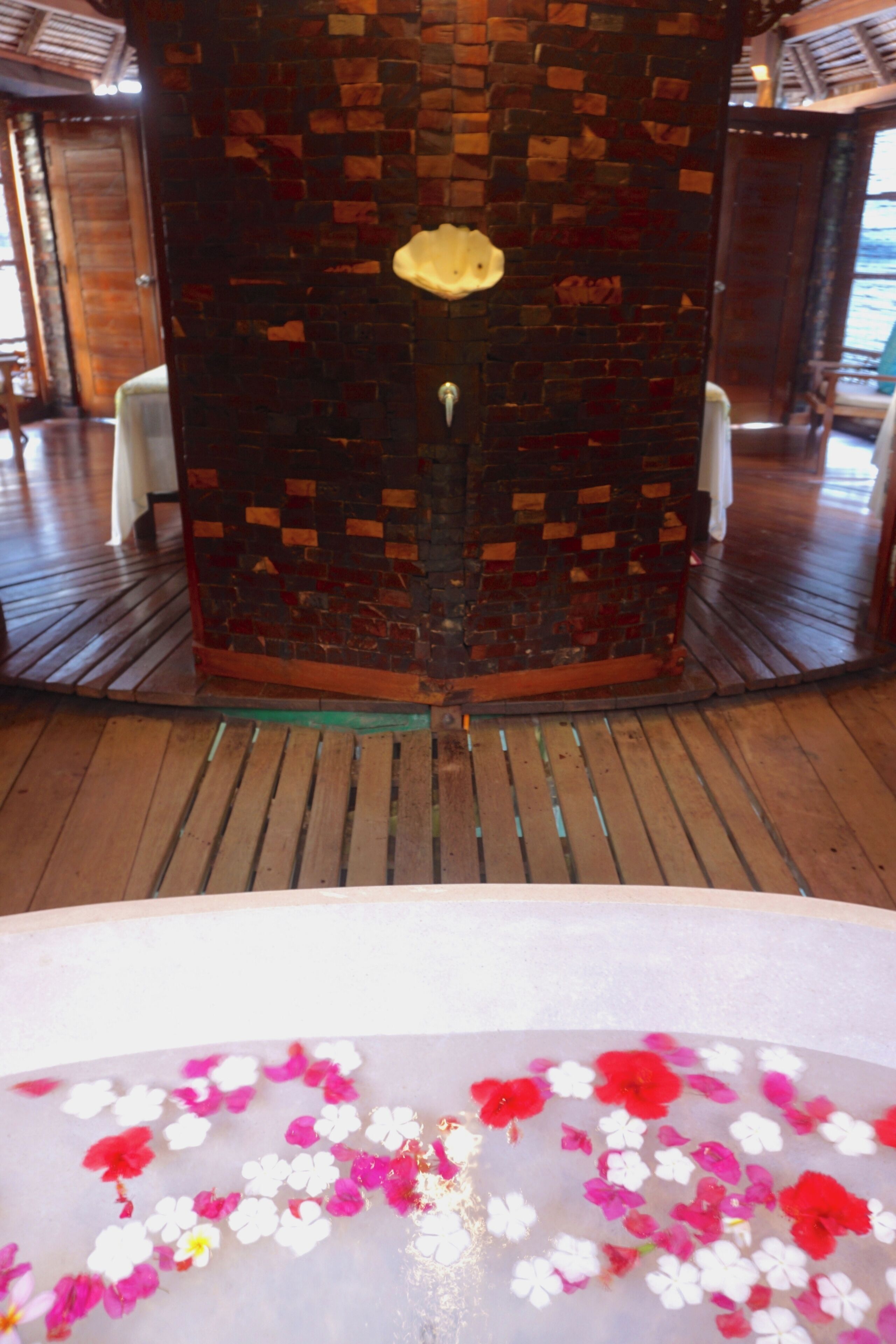 A room with a wooden floor, a brick wall with a small window, and a white chair.