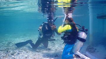 Two divers underwater with scuba gear, surrounded by clear water and sandy sea floor.